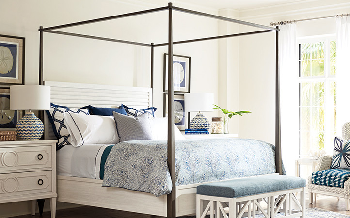 Ocean Breeze bedroom features a king bed with white headboard dark posts alongside two nightstands, a bench, and a chair.
