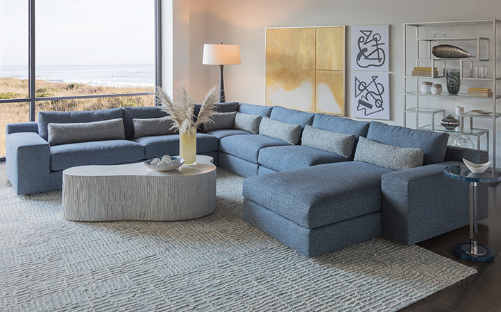 Artistica Upholstery scene featuring a blue sectional, a silver bookcase, one accent table and a cocktail table.